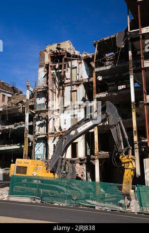 Escavatore di fronte al vecchio edificio in stile architettonico in fase di demolizione. Foto Stock