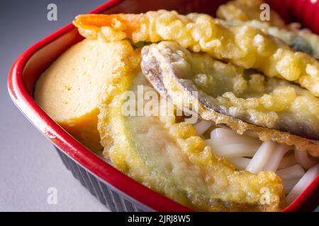 Prelievo da vicino Udon Bento in contenitore per alimenti. I condimenti sono cipolla verde, uova fritte giapponesi (Tamagoyaki), Tempura vegetale e Tempura di gamberi. Foto Stock