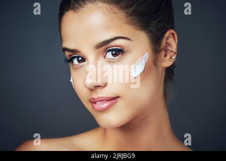 Mantenere la pelle idratata per mantenerla sana. Studio shot di una bella giovane donna con idratante sul viso mentre si posa contro un blu Foto Stock