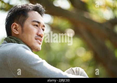 ritratto all'aperto di un giovane uomo asiatico adulto, vista laterale Foto Stock