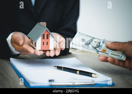 Mani che danno il modello di casa ad altre mani con soldi. Concetto di bene immobile. Foto Stock