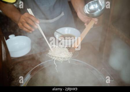 le mani scolano le tagliatelle bollite con un setaccio e dei bastoncini Foto Stock