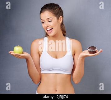 La scelta sana è la scelta più saggia. Studio shot di una giovane donna che sceglie tra cibi sani e non sani su uno sfondo grigio. Foto Stock