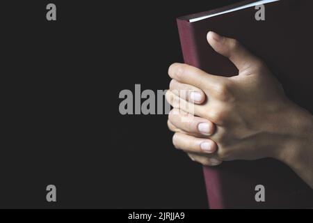 Mani piegate in preghiera su una Sacra Bibbia in concetto di chiesa per la fede, la spiritualità e la religione, il culto, i peccati e la preghiera. Foto Stock