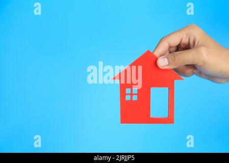 Mano dell'investitore. Uomo d'affari in possesso di una casa rossa. Sfondo blu. Concetto di bene immobile. Ipoteche, investimenti, leasing, acquisto, vendita e manutenzione Foto Stock