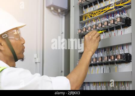 Un elettricista maschio lavora in un pannello di controllo con collegamenti elettrici che collegano dispositivi con un complesso strumento di concetto di lavoro. Foto Stock