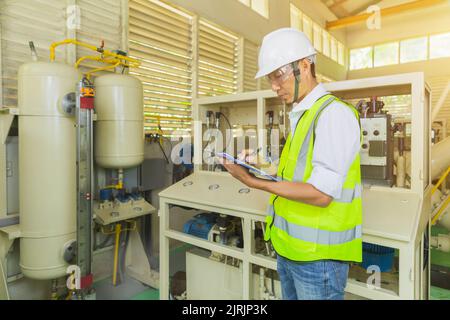 Un tecnico in assistenza tiene una clipboard durante il controllo e la presa di appunti sull'armadio elettrico. Foto Stock