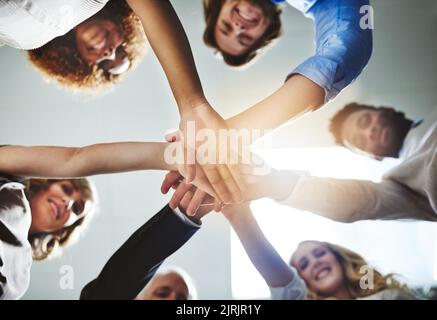 Quando andiamo tutti in noi tutti vincere. Inquadratura a basso angolo di un gruppo di colleghi che si uniscono alle mani in solidarietà. Foto Stock