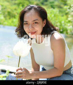 Giovane donna vietnamita sorridente e odora un loto bianco in Vietnam Foto Stock