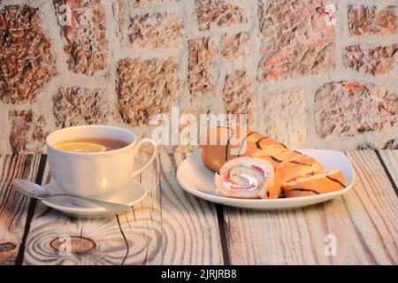 I pezzi di biscotto rotolano con crema e una tazza di tè caldo con una fetta di limone su un tavolo di legno. Primo piano. Foto Stock