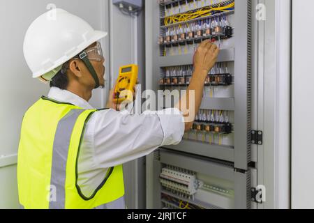 Elettricista che installa i fili dei cavi elettrici e la scatola di commutazione dei fusibili. Multimetro nelle mani dei dettagli degli elettricisti. Foto Stock