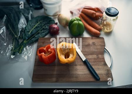 Utilizzando solo gli ingredienti più freschi. Inquadratura ad angolo alto di peperoni tritati su un tagliere circondata da varie verdure su un bancone da cucina. Foto Stock