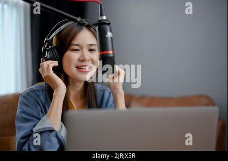 Attraente e allegro giovane donna asiatica podcaster influencer blogger fare podcast audio per il suo canale in casa studio. Foto Stock