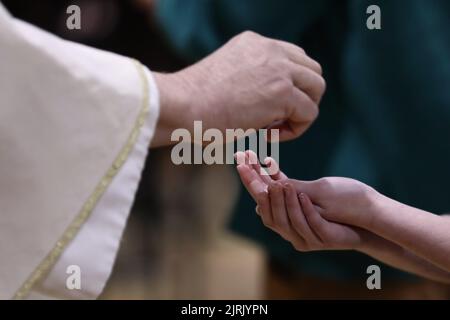 Un sacerdote che sta per mettere il pane ospite o il wafer eucaristico nelle mani di un parrocchiano in una liturgia di massa o in una cerimonia della chiesa. Servire la comunione Foto Stock