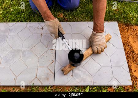 Il padrone stende le pietre di pavimentazione in strati. Percorso di pavimentazione di mattoni di giardino. Posa di lastre di pavimentazione in cemento nel cortile della casa su base di fondazione sabbia Foto Stock