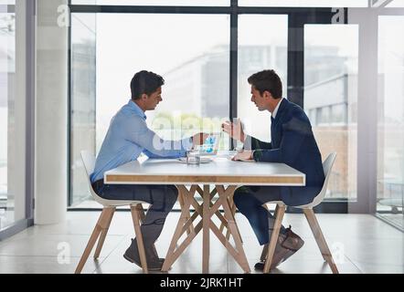 Le competenze collaborative sono essenziali per il successo. Due uomini d'affari che utilizzano un tablet digitale durante una riunione in ufficio. Foto Stock