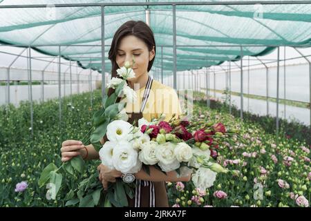 Fiorista donna ha un ordine di fiori freschi. Fa un bel bouquet nella casa verde. Foto Stock