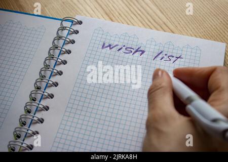 Elenco dei desideri delle parole nel notebook. Mano che tiene la penna e scrivere la lista dei desideri. Desiderio e concetto di sogno. Progettare idee future. Foto Stock