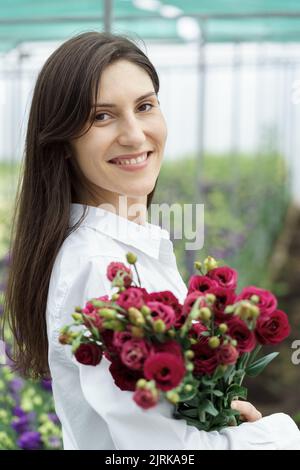 Donna d'affari tiene un bel bouquet nella casa verde. Donna ritratto con fiori. Fiorista femminile ha un ordine di fiori freschi. Foto Stock