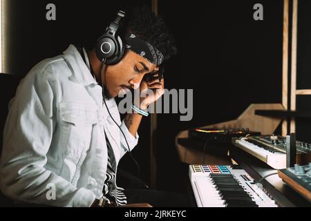 Musicista maschio afro-americano che suona il pianoforte elettrico mentre prova la musica in studio di registrazione Foto Stock