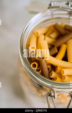 Primo piano vaso di vetro riempito con diversi colori di pasta sul tavolo Foto Stock