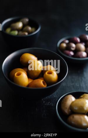Dall'alto gustose e succose olive verdi gialle in ciotole bianche e nere su tavola nera decorata con Foto Stock