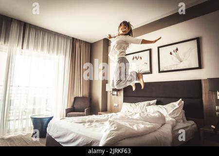 Donna che si diverte e che salta con l'accappatoio sul letto in camera d'albergo Foto Stock