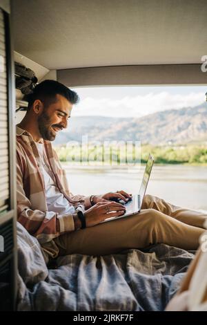 Contenuto uomo ispanico che lavora sul computer portatile mentre si siede in camper durante il viaggio Foto Stock