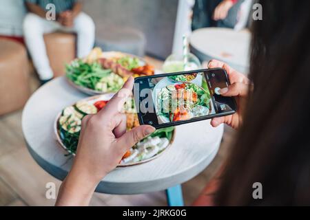 Dall'alto del raccolto irriconoscibile vlogger femmina che scatta foto di delizioso power ciotola sul cellulare in ristorante Foto Stock
