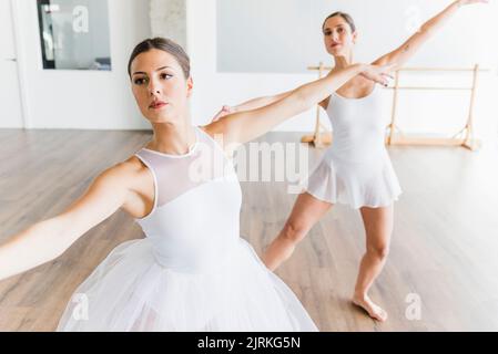 Due eleganti ballerine giovani che ballano in sincronia accanto ad uno specchio in una sala da ballo Foto Stock