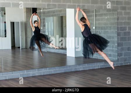Foto in bianco e nero di una giovane ballerina che fa un salto di fronte ad uno specchio in studio di danza Foto Stock