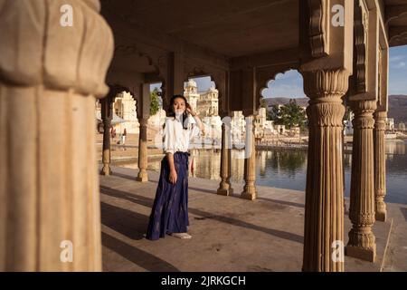 Corpo pieno donna asiatica guardando lontano mentre si trova sotto il tetto di edificio ad arco sulla costa del Lago Sacro Pushkar in Rajasthan, India Foto Stock