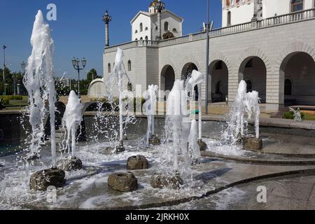 Spruzzi d'acqua da una fontana sullo sfondo di una chiesa bianca. Struttura naturale di acqua di fontana. Effetto delle onde alte nell'estate calda Foto Stock