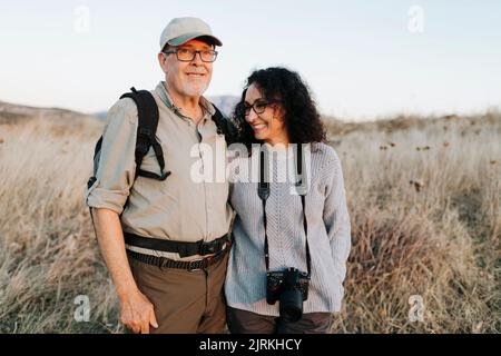 Coppia matura allegra in abiti casual abbracciando e in piedi su prato erboso in campagna Foto Stock