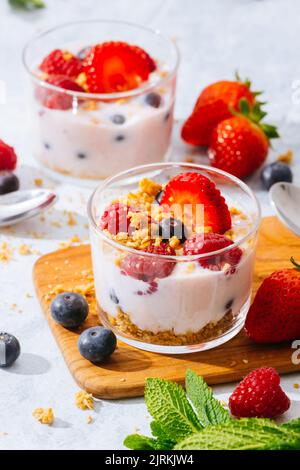 Delizioso yogurt fatto in casa con fragole, frutti di bosco e cereali su sfondo bianco Foto Stock