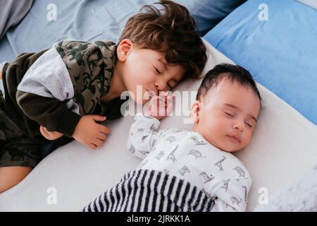 Dall'alto di un piccolo ragazzo affascinante abbracciare piccolo fratello mentre dormono pacificamente insieme in un comodo letto Foto Stock