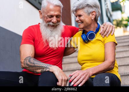Angolo inferiore di una coppia anziana seduta su una rampa di scale mentre si abbraccia dopo aver giocato sport in strada Foto Stock