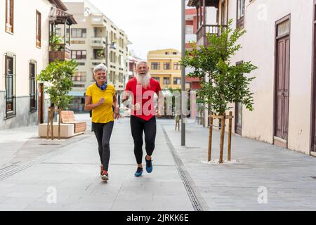 Vista frontale di una felice coppia senior che corre in città Foto Stock