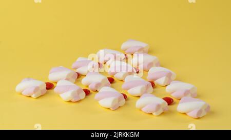 Marshmallow e dragee di caramelle rosse sotto forma di triangolo su sfondo giallo Foto Stock