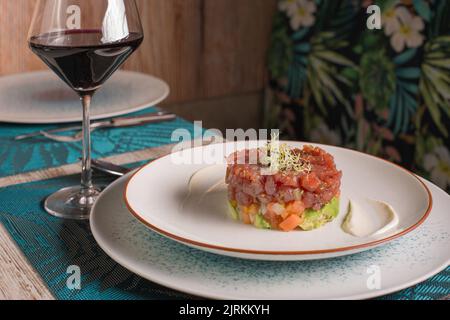 Tartare gourmet di tonno rosso con salsa su piatto servito con un bicchiere di vino rosso sul tavolo nel ristorante Foto Stock
