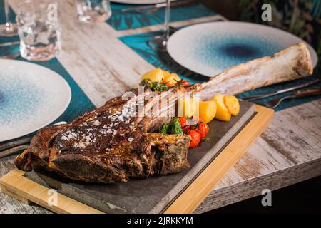 Gustosa bistecca di manzo ribeye alla griglia con grani di sale e pomodori rossi e gialli luminosi sul tavolo servito Foto Stock