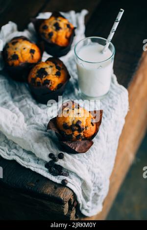 Deliziosi muffin con gocce di cioccolato e un bicchiere di latte su sfondo di legno scuro Foto Stock