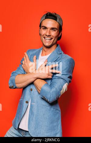 Giovane uomo alla moda in abbigliamento alla moda e cappuccio che mostra un gesto rap mentre si guarda la fotocamera Foto Stock