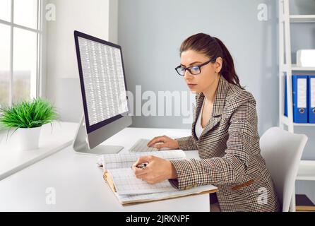 Il contabile femminile concentrato confronta i dati in fogli di calcolo e in contabilità cartacea. Foto Stock