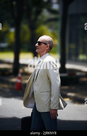 Imprenditore anziano in occhiali da sole a piedi per strada Foto Stock