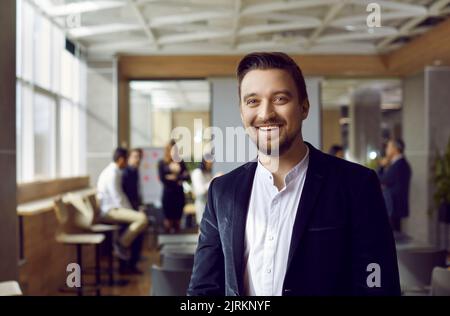 Ritratto di gioioso uomo d'affari soddisfatto su sfondo sfocato di persone in ufficio. Foto Stock
