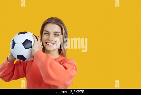 Giovane donna sorridente con classica palla di calcio bianca e nera in mano su sfondo banner. Foto Stock