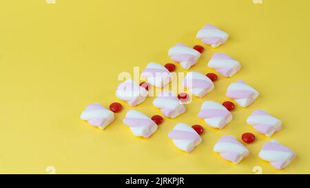 Marshmallow e dragees di caramelle rosse allineati con un albero di Natale Foto Stock