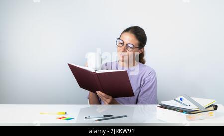 Una ragazza legge un libro o un libro di testo e beve caffè - studio, compiti Foto Stock