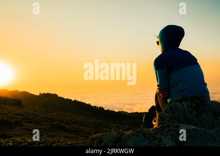 Sole felice donna ritratto guardare alba. Donna turistica spensierata guardando il sole godendo il paesaggio. Ragazza viaggiatore in cima alla montagna in raggi di sole Foto Stock